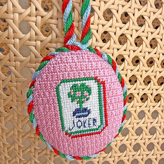 Pink embroidered egg with 'Joker' design on a woven surface