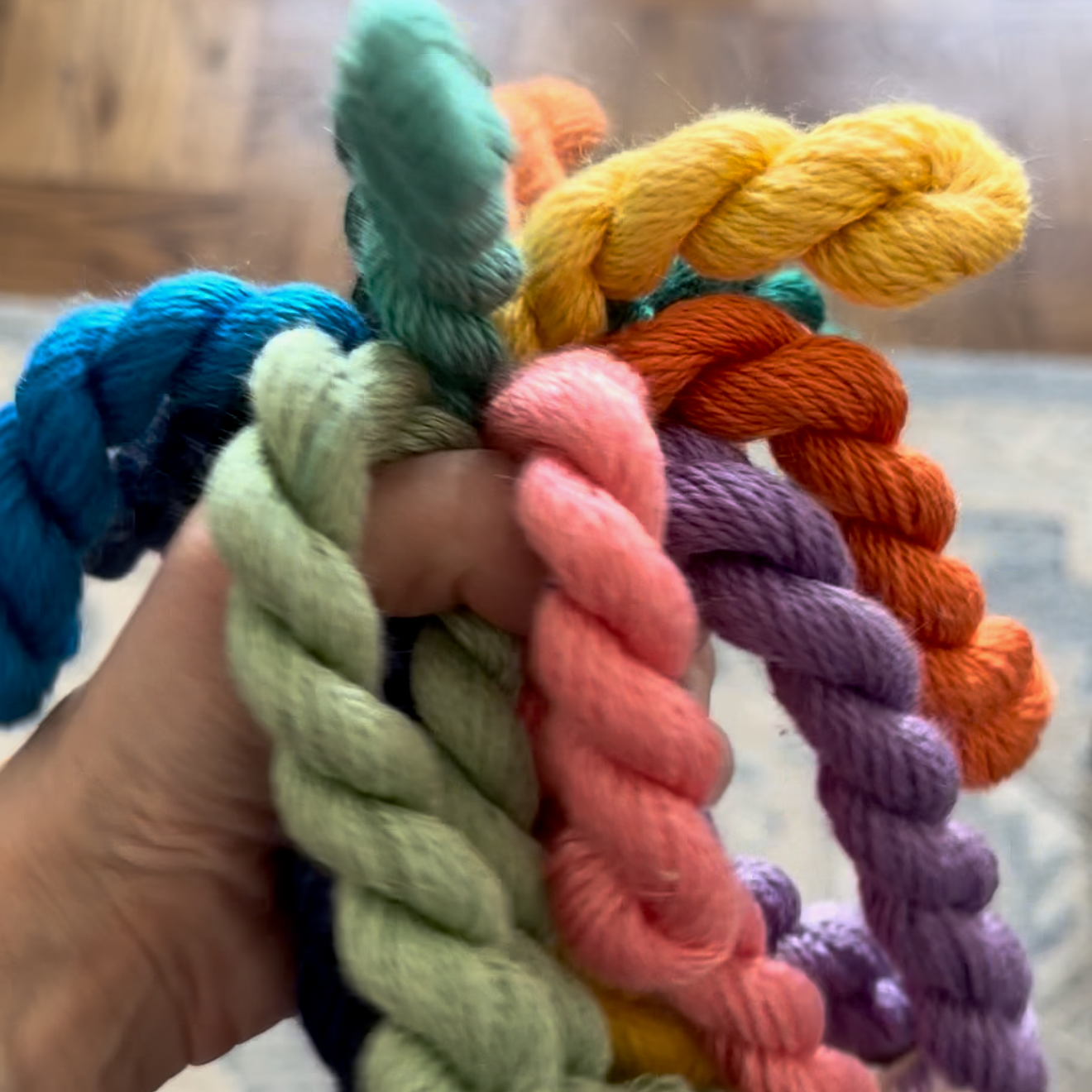 Colorful braided yarn held by a hand against a neutral background